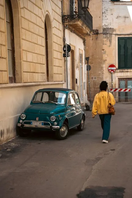Petite voiture ancienne verte garée, passante en veste jaune à Lecce