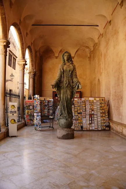 Green statue surrounded by postcard racks under Lecce arcade