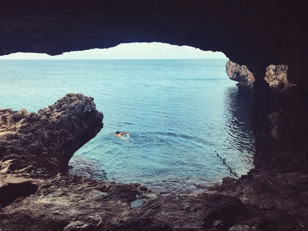 Bather swimming from a cave out to the Salento sea