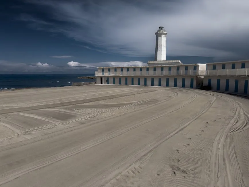 Empty sandy beachfront with tire marks and Lecce lighthouse in the distance