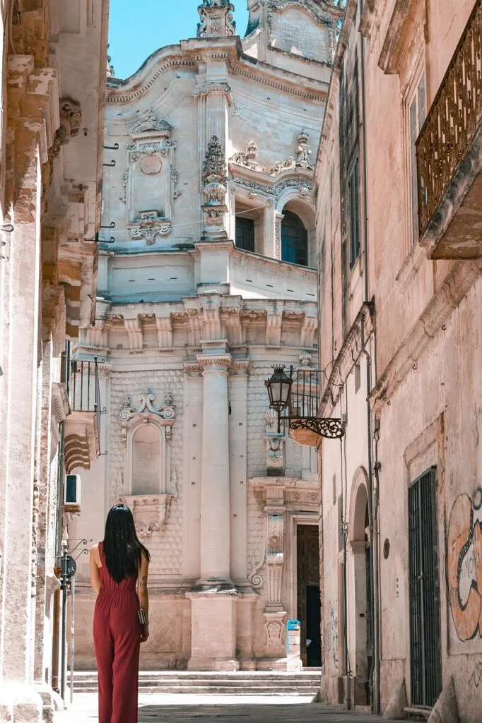 Person admiring tall Baroque columns of Lecce church from alley