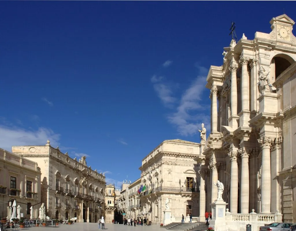 Sunlit Lecce piazza flanked by a grand Baroque cathedral and buildings.