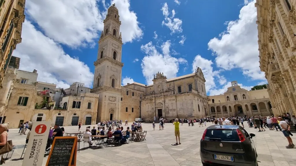 Lecce's main square with its cathedral, bell tower and tourists under a blue sky