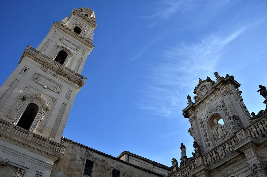 Tall bell tower and ornate Baroque facade silhouetted against Lecce sky